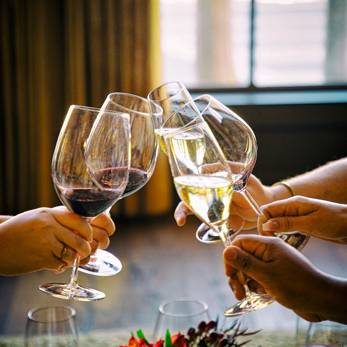 Five wine glasses being clinked together at a table with a blurred background
