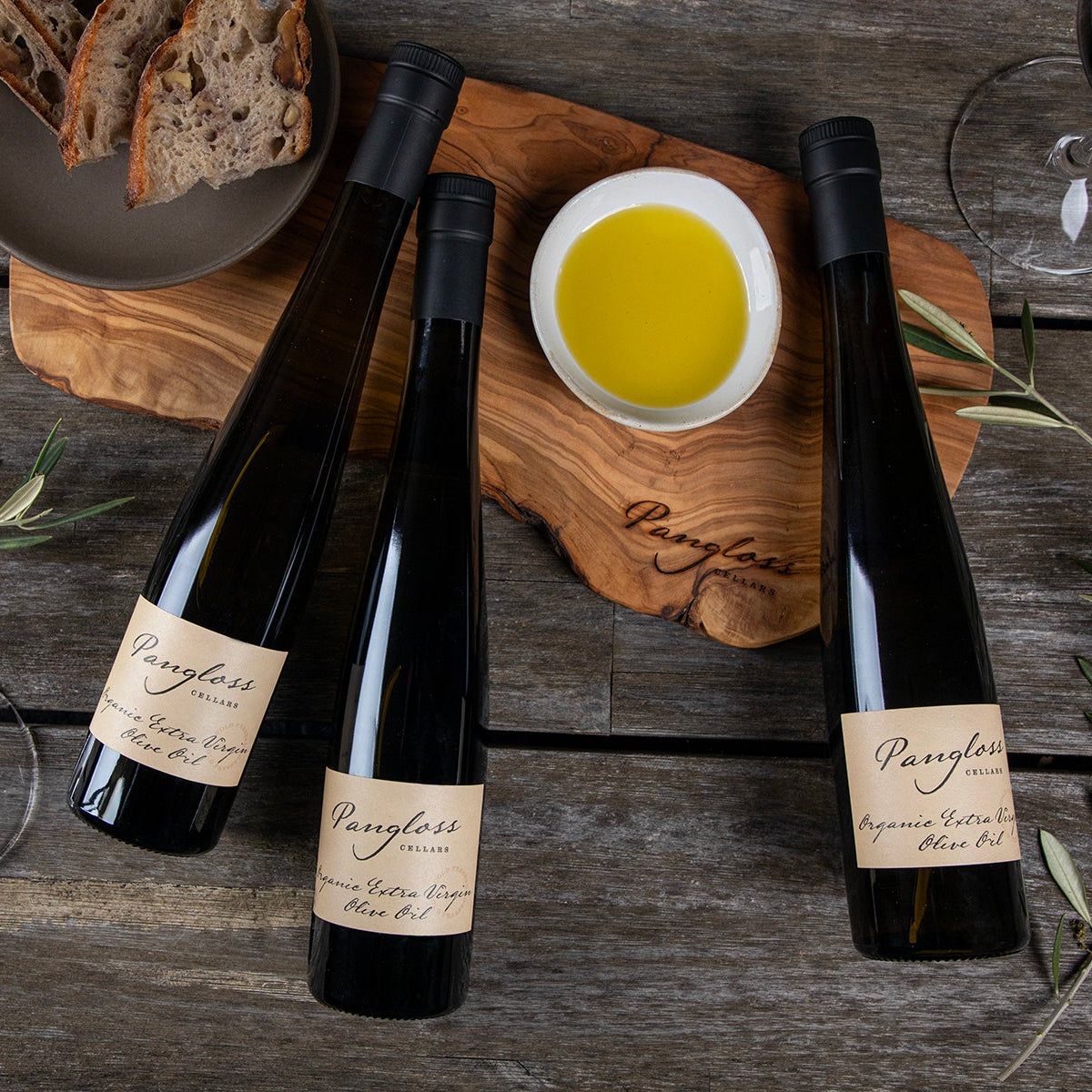 Three wine bottles on a wooden surface with olive oil and bread.