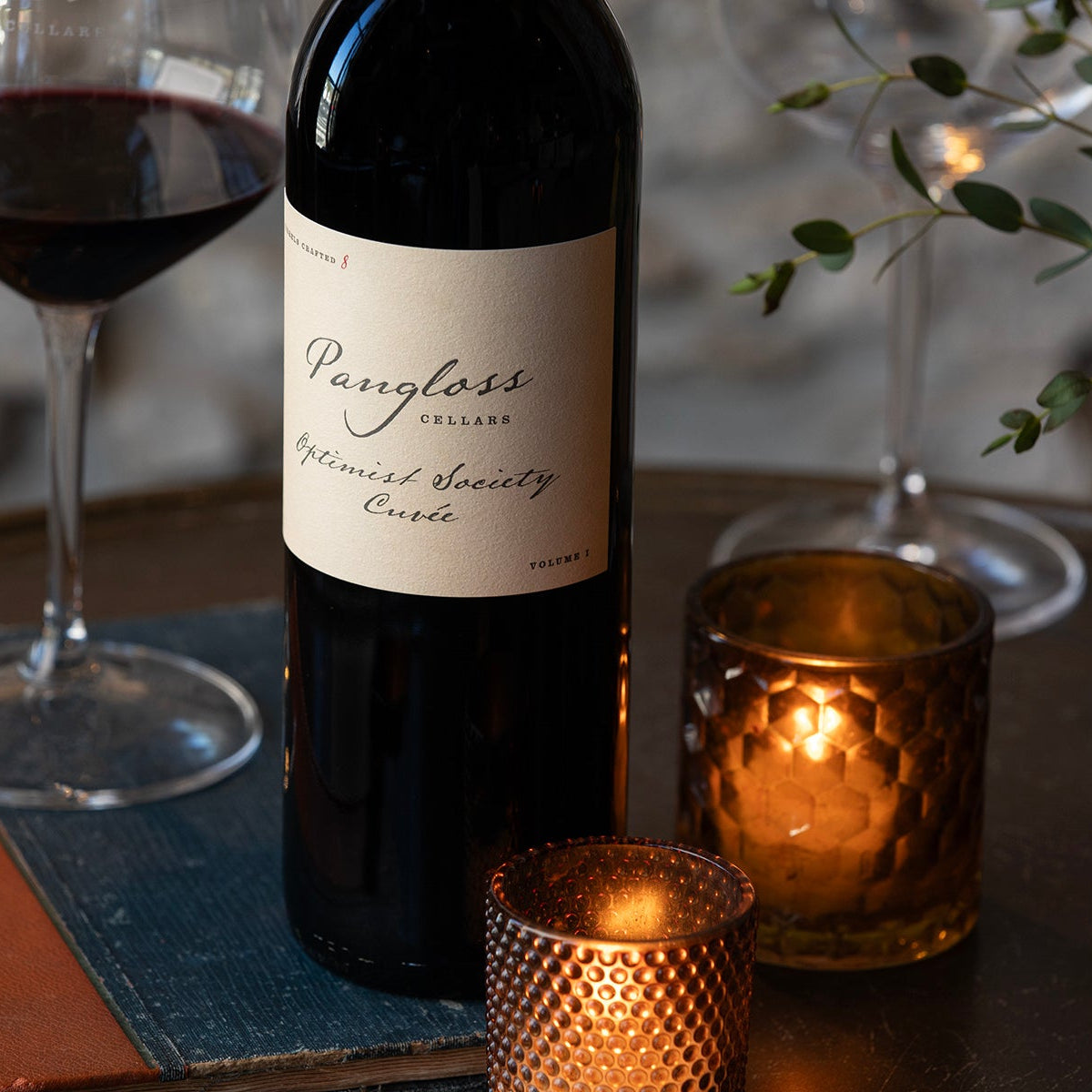 Red wine bottle with a glass of wine on a table with candles and a book.