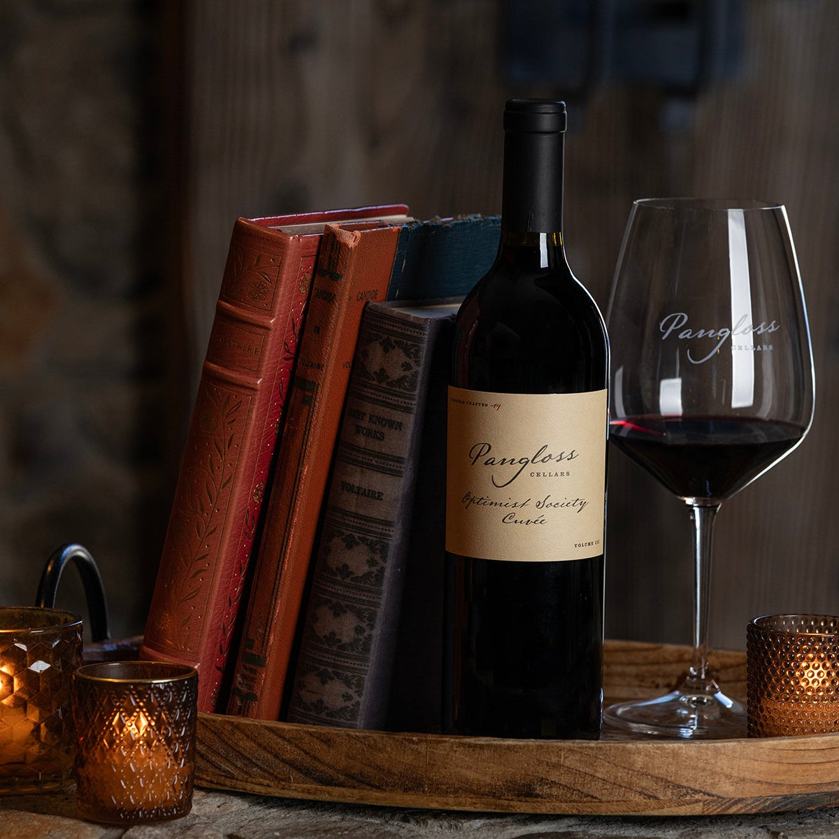 Wine bottle and glass on a wooden tray with candles and books in a warm setting