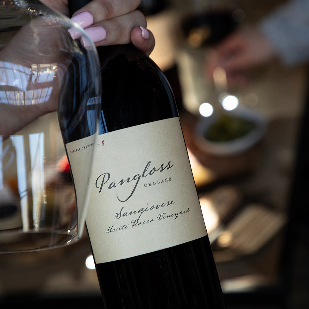Wine bottle with Pangloss label held by a hand, blurred background