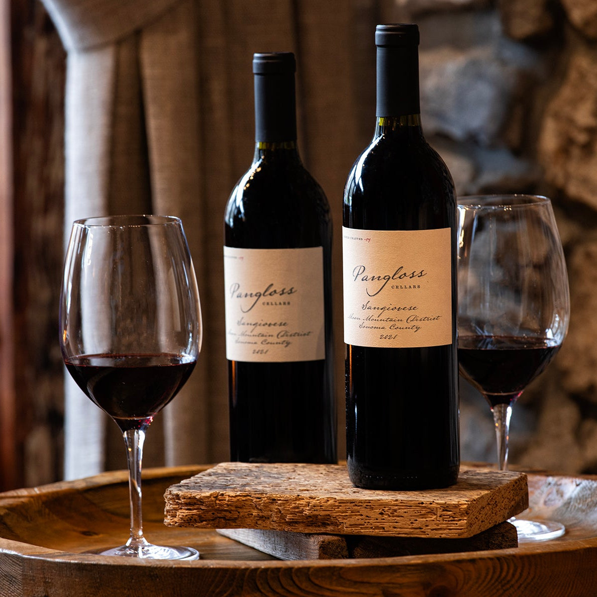 Two bottles of wine and two glasses on a wooden tray with a stone wall background