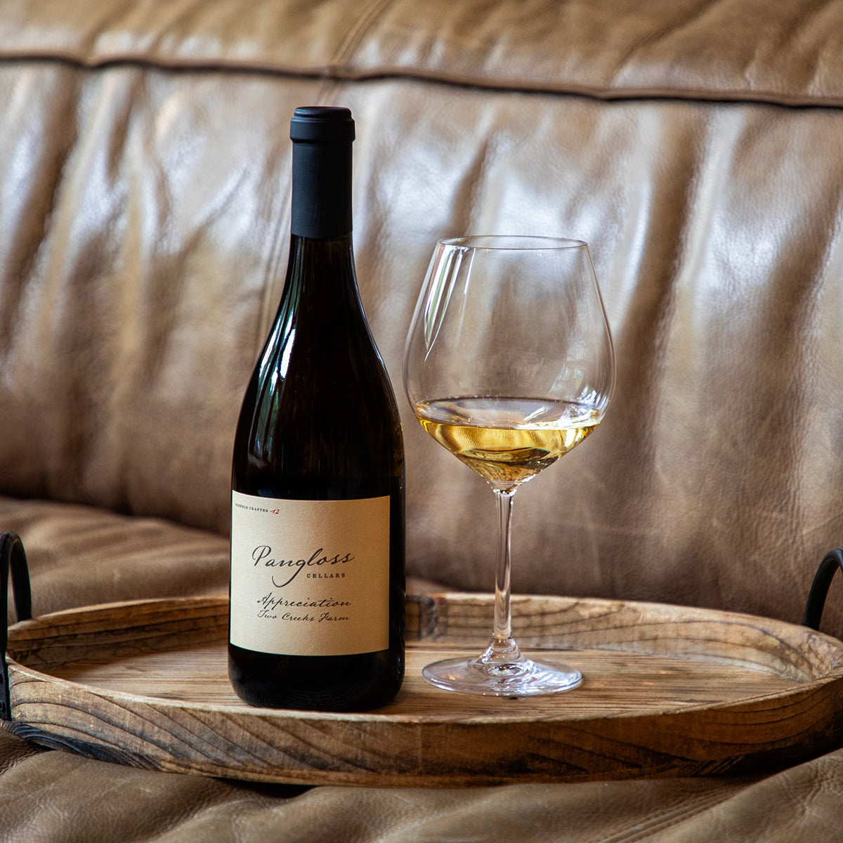 Bottle of wine and glass on a wooden tray with a brown leather couch background