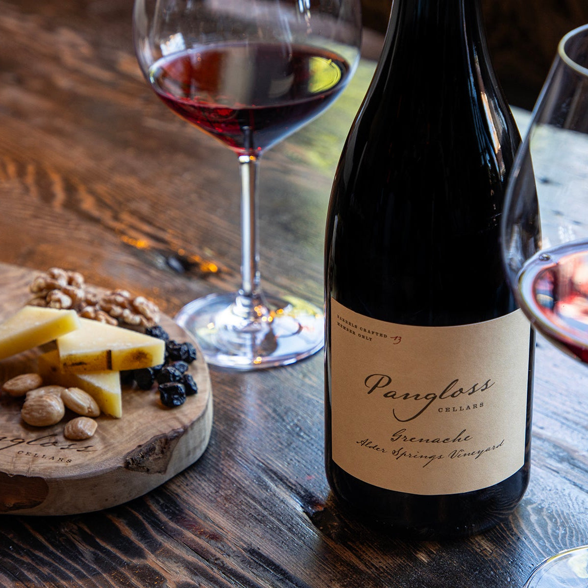 Wine bottle with two glasses of red wine and a charcuterie board on a wooden table.