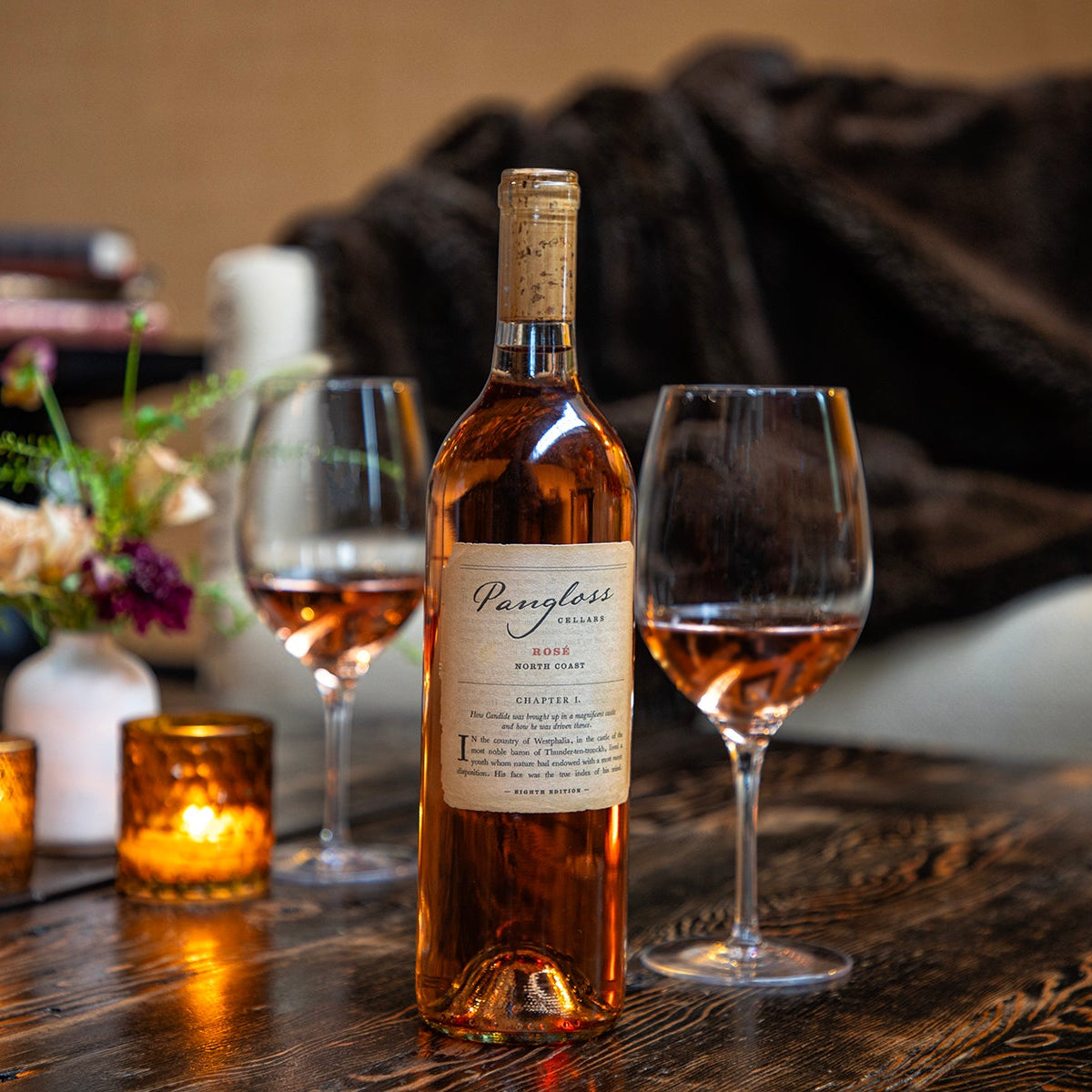 Wine bottle and glasses on a wooden table with candles and flowers in the background