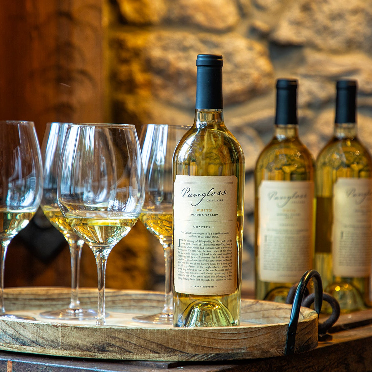 Wine bottles and glasses on a wooden tray with a stone wall background
