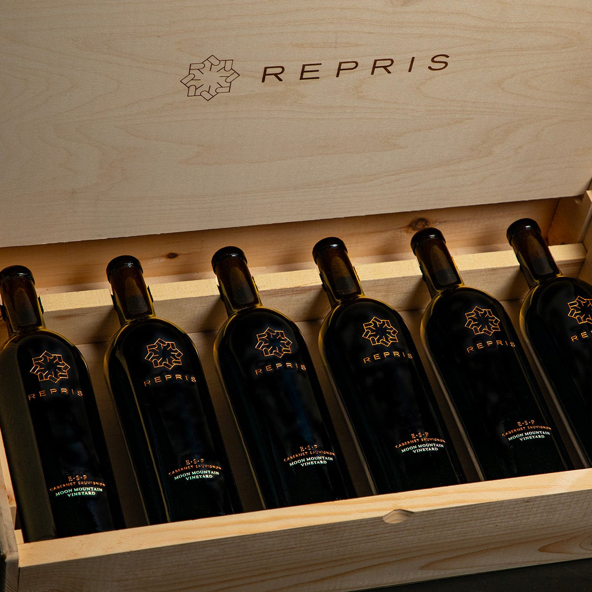 Wooden box with six bottles of wine labeled 'Repris' on a dark background