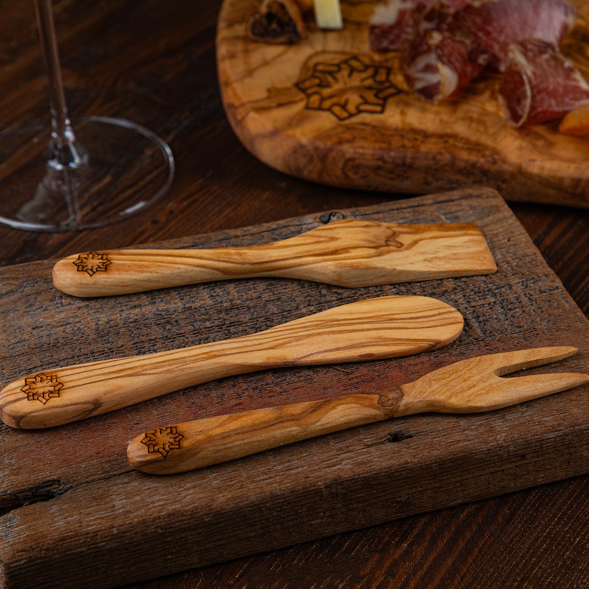 Wooden cheese knives on a wooden board with a charcuterie board in the background.