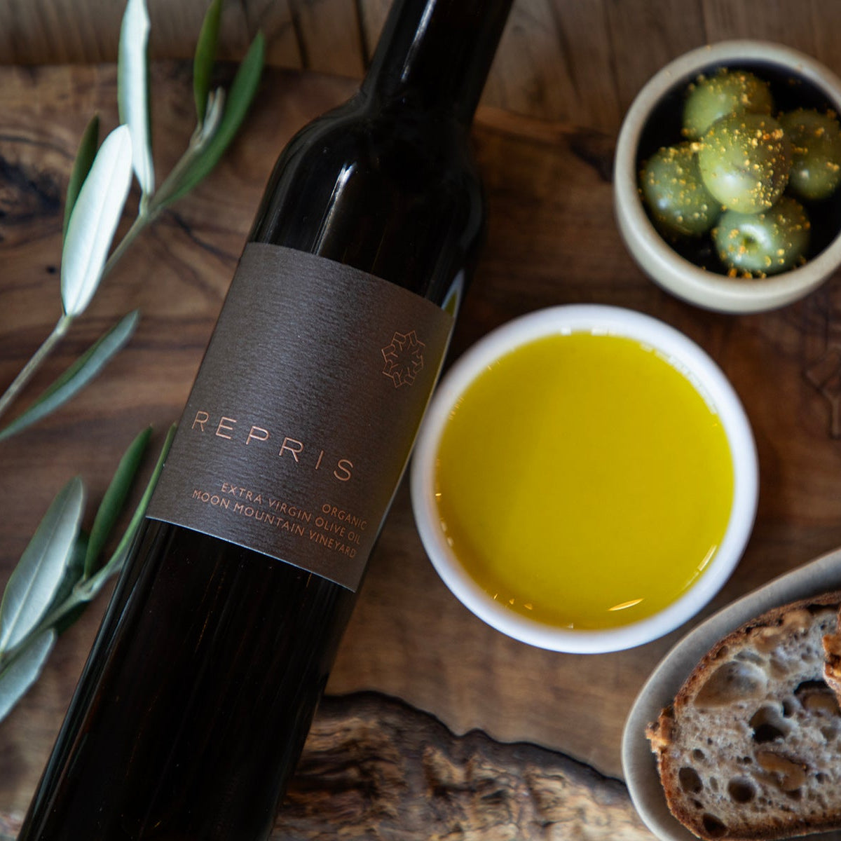 Bottle of Repris wine with olive oil, bread, and olives on a wooden surface